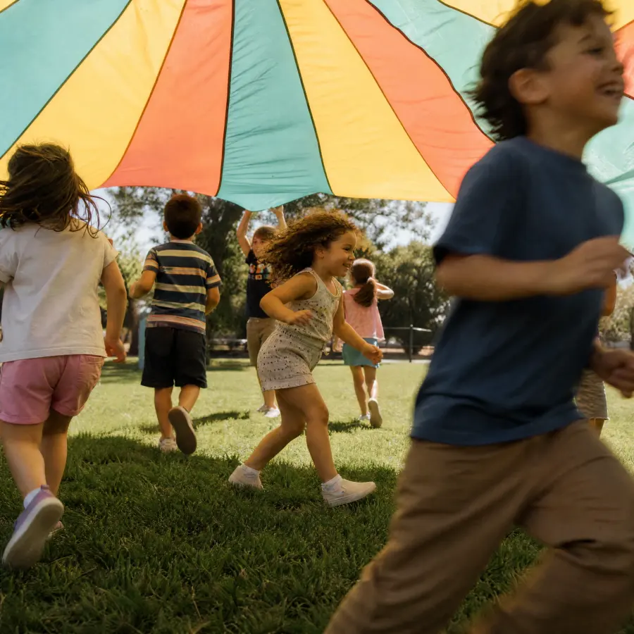 Children playing under a rainbow parachute at summer camp